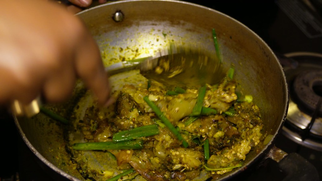 कढईत ठेचलेलं वांगं आणि कांद्याची पात मसाल्यात एकजीव करणे